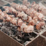 Costelão bovino assando lentamente em espetos fincados na terra ao redor de brasas