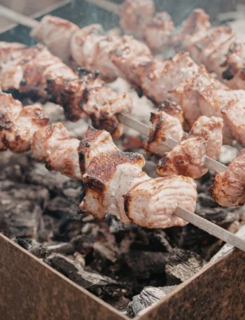 Costelão bovino assando lentamente em espetos fincados na terra ao redor de brasas