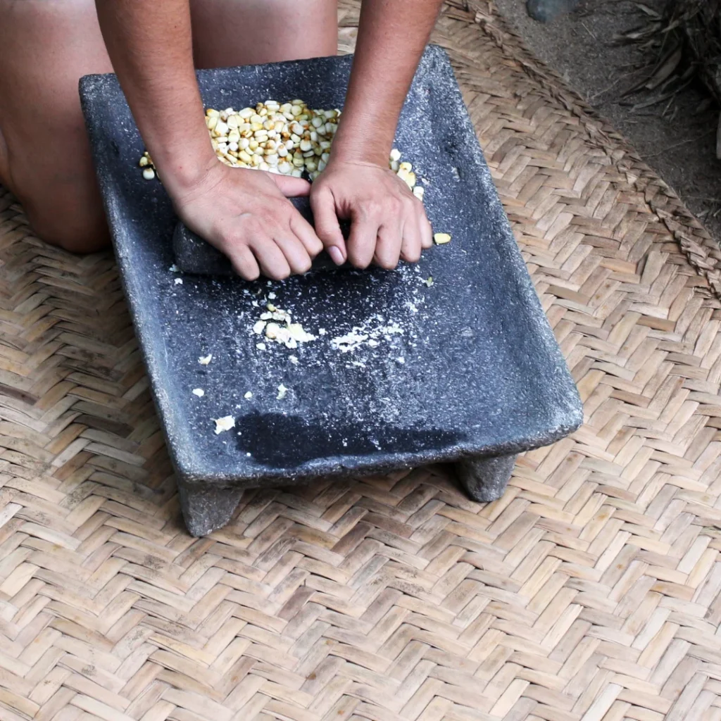 Mãos de uma mulher mexicana moendo milho nixtamalizado em um metate de pedra vulcânica