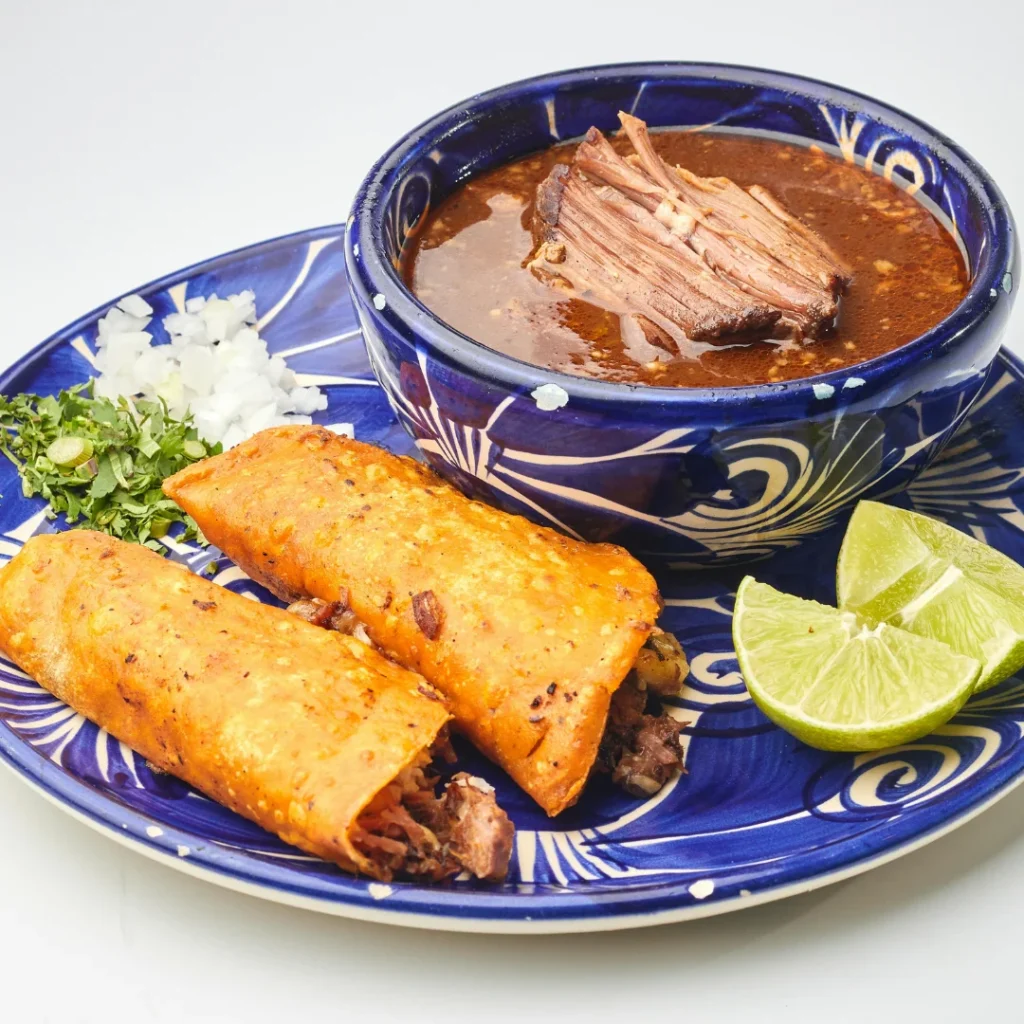 Mesa com tacos, tamales e uma tigela de pozole fumegante em ambiente rústico