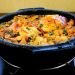 Panela de barro fumegante recheada com peixe, camarões, pimentões coloridos e coentro fresco.