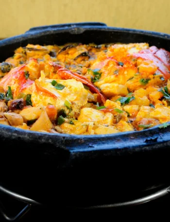 Panela de barro fumegante recheada com peixe, camarões, pimentões coloridos e coentro fresco.