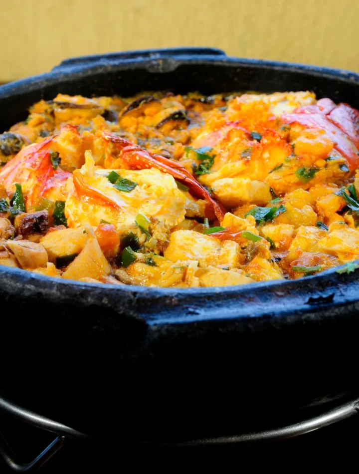 Panela de barro fumegante recheada com peixe, camarões, pimentões coloridos e coentro fresco.