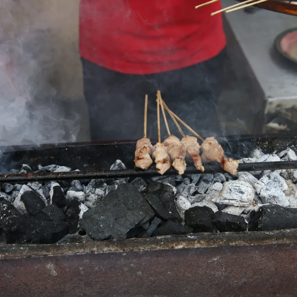 Pequenos espetos de frango sendo grelhados em uma churrasqueira japonesa estreita com brasas vivas