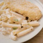 Prato farto de frango frito dourado servido ao lado de macarrão com queijo cremoso