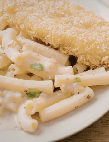 Prato farto de frango frito dourado servido ao lado de macarrão com queijo cremoso